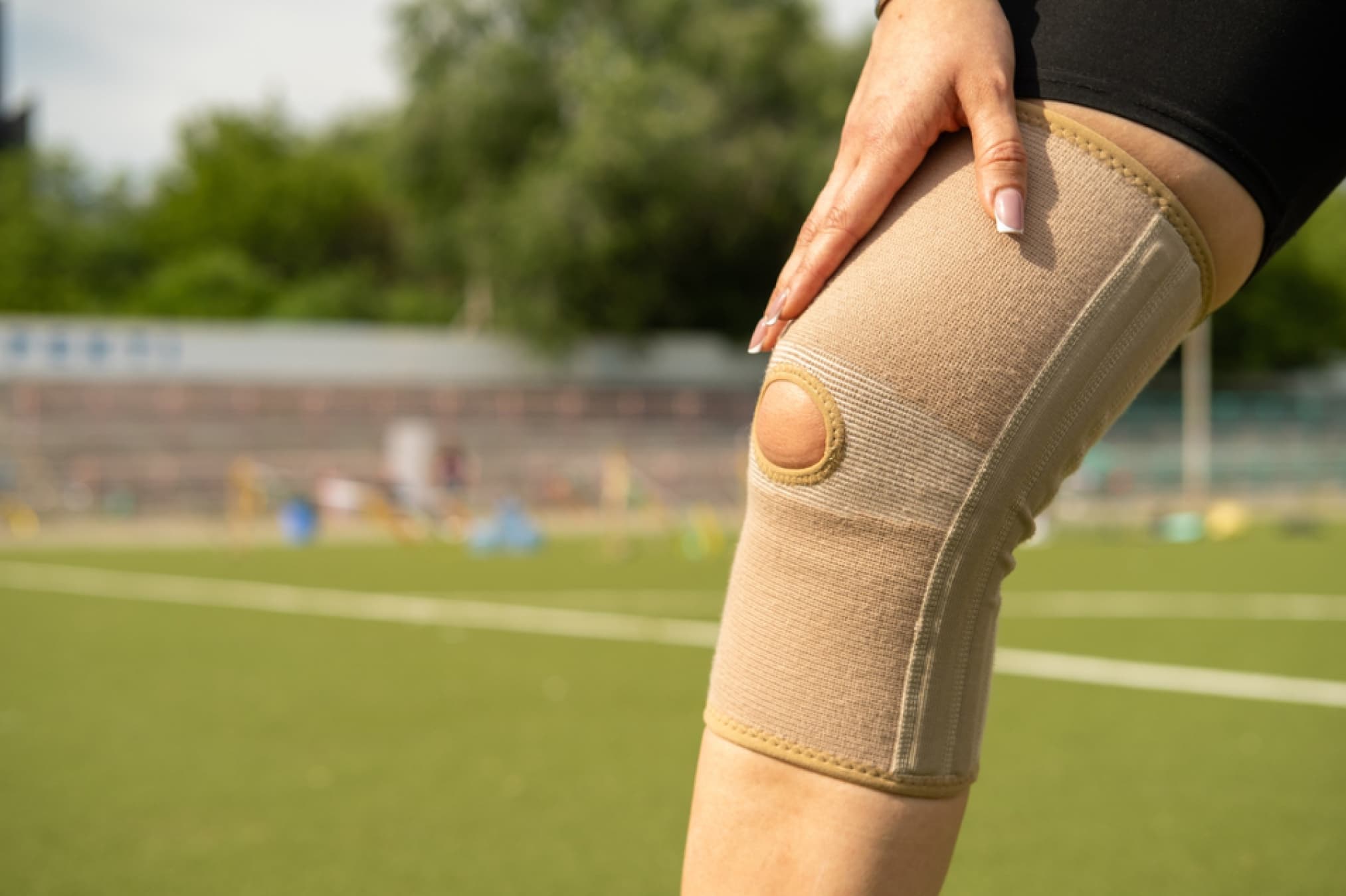 Person holding their knee, wearing a supportive knee brace on a sports field