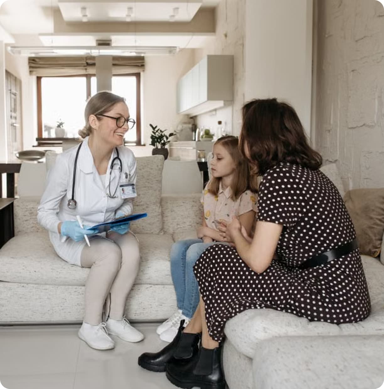 Clinician in a white coat talking with a mother and daughter at home